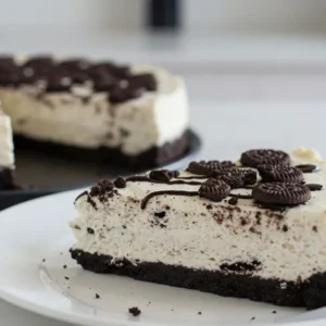 A close-up shot of a creamy, no-bake Oreo cheesecake topped with crumbled Oreos and whole cookies. The rich, velvety texture of the filling is visible, with the Oreo crust adding a tempting contrast.